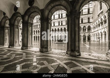 Blick (in Sepia) durch die Bögen in den Innenhof des Dogenpalastes in Venedig, wo der nordbronzene Brunnen zu sehen ist. Stockfoto