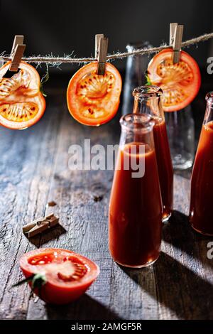 Tomatenscheiben hingen an einer Schnur.Tomatensaft in Glasflaschen.Frisches Getränk und Essen. Stockfoto