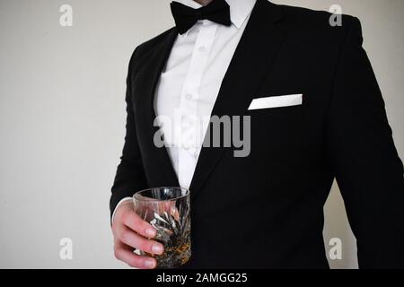 Nahaufnahme eines Mannes in einem schwarzen Tuxedo, der ein Whiskyglas hält Stockfoto