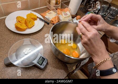 Paar Hände Mischen einer Kuchenmischung mit Eiern in einer Schüssel mit Orangen und Mandeln. Stockfoto
