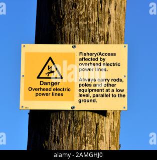 Warnschild für die Elektrizität über dem Kopf an einem Holzmast, Großbritannien Stockfoto
