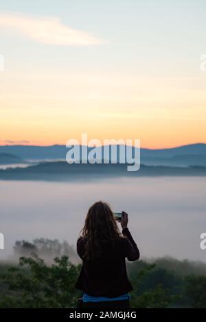 Frau, die auf ihren Telefonbergen ein Bild von Sonnenaufgang macht Stockfoto