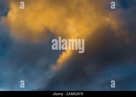 Flauschige Wolken, die durch verschwindende Strahlen bei Sonnenuntergang und dunkle Gewitterwolken erhellt werden, die über sonnigen blauen Himmel schweben, um das Wetter in der Saison zu ändern. Fantastische Aussicht Stockfoto