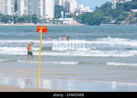 Rotes Warnschild am Strand. Bord, die raue oder tiefe See signalisieren. Plaque geschrieben in brasilianischem portugiesisch, PERIGO. Foto in Praia da Enseada - Gu Stockfoto