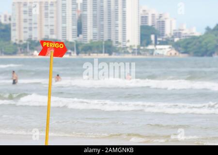 Rotes Warnschild am Strand. Bord, die raue oder tiefe See signalisieren. Plaque geschrieben in brasilianischem portugiesisch, PERIGO. Foto in Praia da Enseada - Gu Stockfoto