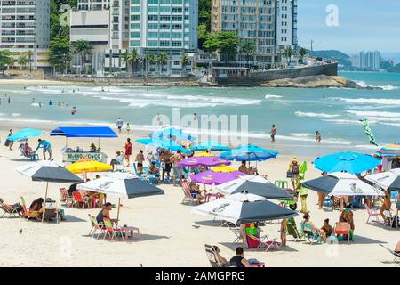 Guaruja - SP, Brasilien - 20. November 2019: Sonnenanbeter am Strand Praia das Pitangueiras, dem wichtigsten städtischen Strand der Stadt. Gebäude von Morro da Stockfoto
