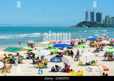 Guaruja - SP, Brasilien - 20. November 2019: Sonnenanbeter am Strand Praia das Pitangueiras, dem wichtigsten Touristenstrand der Stadt. Gebäude von Jardim Asturias Stockfoto