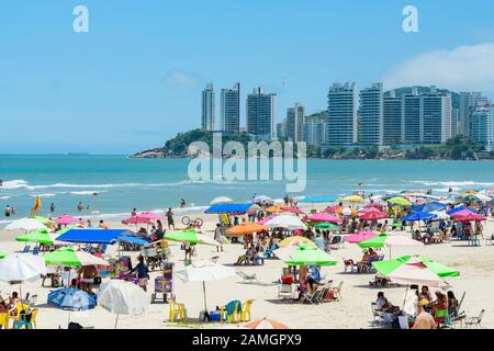 Guaruja - SP, Brasilien - 20. November 2019: Sonnenanbeter am Strand Praia das Pitangueiras, dem wichtigsten Touristenstrand der Stadt. Gebäude von Jardim Asturias Stockfoto