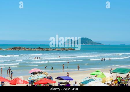 Guaruja - SP, Brasilien - 20. November 2019: Sonnenanbeter am Strand Praia das Pitangueiras. Blick auf den Strand, die Insel Ilha Pompeba in der Mitte und die Stockfoto