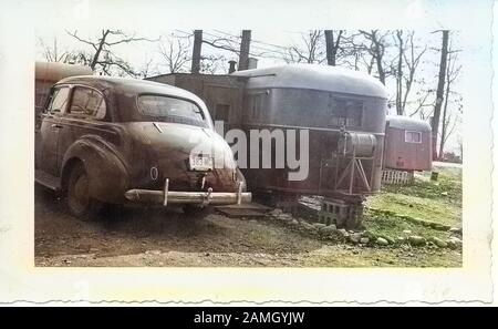 Schwarz-Weiß-Foto, das einen alten Chevrolet-Limousinen-Wagen zeigt, mit einer Ohio-Lizenz vom Jahr 1945, die außerhalb, in einer winterlichen Landschaft geparkt ist, mit ein paar Karawanen oder gezogenen Anhängern im Hintergrund, wahrscheinlich fotografiert in Ohio im Jahrzehnt nach dem zweiten Weltkrieg 1950. Hinweis: Das Bild wurde mit einem modernen Verfahren digital koloriert. Farben sind möglicherweise nicht periodengenau. () Stockfoto