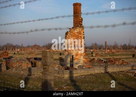 Auschwitz- Birkenau, Polen- Elektrozaun mit Stacheldraht, zerstörte Kasernen, Gaskammern und Ziegelsteinkrematoriumsschornsteine im Konzentrationslager Stockfoto