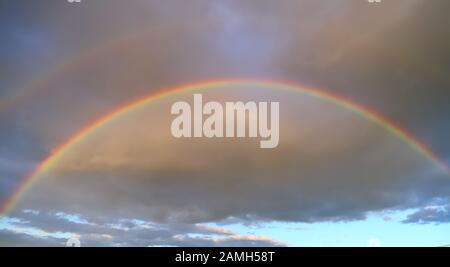 Voller doppelter Regenbogen am Himmel vor dem Hintergrund von Wolken Stockfoto