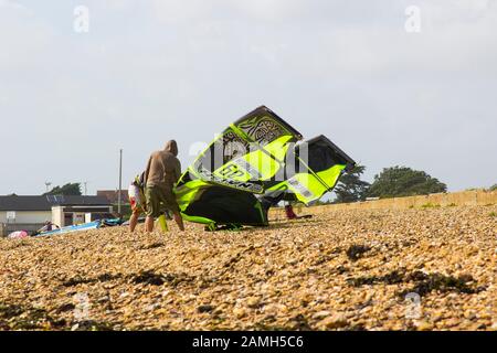 Juni 2017 KÄMPFEN EIN paar junge Männer gegen eine steife Brise, um ihren Para-Segelflugzeug für einen Nachmittagssport am Strand in Titchfield, Ham, vorzubereiten Stockfoto