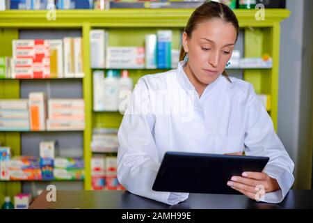 Lächelnd glücklich, selbstbewussten jungen Frau Apotheker arbeiten an einem Schreibtisch in der Apotheke Stockfoto
