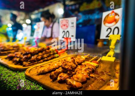 Bangkok/Thailand-05 Dezember 2019: Szenen aus dem Talat Rot Fai Nachtlebensmittelmarkt, mit Schweinefleisch- und Hühnerfleischspießen von geröstetem Fleisch und Preisschildern in Stockfoto