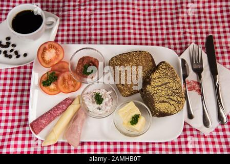 Auf einem roten karierten Tischtuch befindet sich ein Teller mit einem herzhaften Frühstück und einer Tasse schwarzem Kaffee Stockfoto