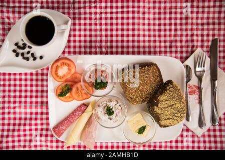 Auf einem roten karierten Tischtuch befindet sich ein Teller mit einem herzhaften Frühstück und einer Tasse schwarzem Kaffee Stockfoto