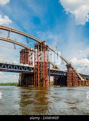 Blick vom Fluss auf eine rostige Brücke an einem sonnigen Tag. Verrosteter, unfertiger Steg in Kiew, Panorama der Ukraine. Stockfoto