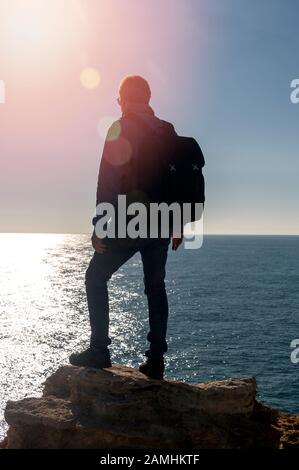 Backpacker, der auf einem Felsen am Meer steht, Linsenflaum. Stockfoto