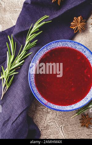 Hausgemachte würzige Süßsoße aus nördlichen Waldbeeren Preiselbeeren und Äpfeln mit Rosmarin, Zimt und Anissternen in blauer Schüssel. Draufsicht Stockfoto