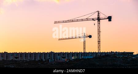 Zwei Baukräne bei Sonnenuntergang über die neu erbaute Wohnanlage in der Nähe von La Tejta Strand. Stockfoto