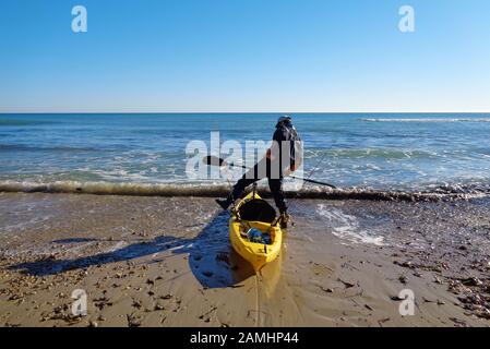 MIL palmeras, Spanien, 11. Januar 2020: Ein Sportler und Fischer, der eine Jacke trägt, steht im Wasser in der Nähe eines Kajakboots. Stockfoto