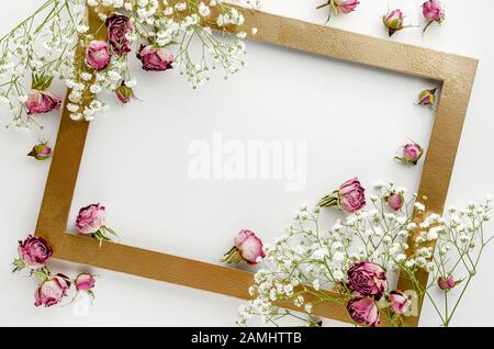 Kreativer goldener Rahmen mit getrockneten rosafarbenen Rosen auf weißem Hintergrund. Grußkartenkonzept. Flaches Layout, Kopierbereich Stockfoto