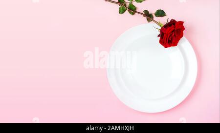 Romantisch gedeckten Tisch für Valentines Tag oder Abendessen Datum Feier Hochzeit. Valentines Tag Konzept mit rote Rose Bud White Platten auf Pastell rosa Tischdecke Hintergrund. Flach, Ansicht von oben kopieren. Stockfoto