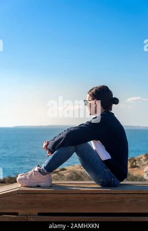 Frau auf einer Holzbank mit Blick auf das Meer Stockfoto