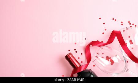 Fröhlicher Valentinstag mit einer Flasche Wein, Champagner, Glas, rotem Band auf pinkfarbenem Hintergrund. Flaches Layout, Draufsicht, Kopierbereich. Valentinstag c Stockfoto