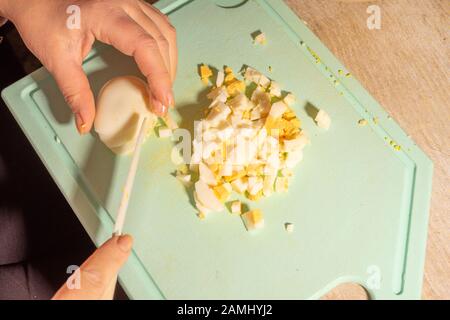 Die Hände des Kochs hacken Eier und Kartoffeln für Salat. Gesundes, natürliches vegetarisches Essen Stockfoto