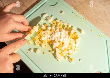 Die Hände des Kochs hacken Eier und Kartoffeln für Salat. Gesundes, natürliches vegetarisches Essen Stockfoto