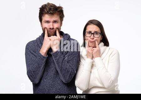 Traurige Frau und Ehemann haben Lebensprobleme, die versuchen zu lächeln, verärgerter junger Mann und Frau, die in Verzweiflung an der weißen Wand verloren wurden. Studio gedreht Stockfoto