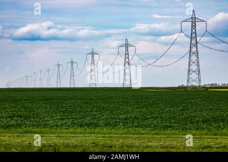 Ein weiter Blick auf Strompflaste mit kilometerlangen Stromleitungen, die viele Hektar ländlicher Ackerflächen abdecken und in weit entfernten Horizont verschwinden Stockfoto