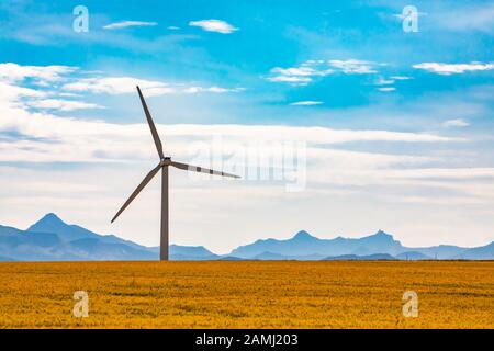 Eine Windenergieanlage mit Maschinenhaus und drei Rotorblättern auf einem Monopol wird über ländlichem Ackerland in Saskatchewan, Kanada, hoch gesehen. Mit Bergen am Horizont Stockfoto