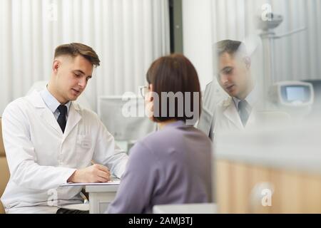 Portrait von gutaussehenden jungen Augenärzten, die während der Beratung in der Klinik mit weiblichen Patienten sprechen, Kopierraum Stockfoto