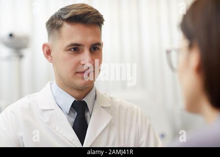 Nahaufnahme des Portraits der gutaussehenden jungen Augenärztin, die während der Beratung in der Klinik weiblichen Patienten zuhört, Kopierraum Stockfoto