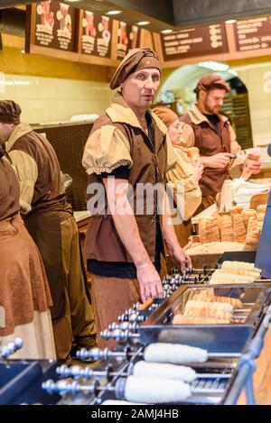 Cooking Trdelnik, ein traditioneller kegelförmiger Blätterteig, der auf einem Holzkegel zubereitet und mit Sahne, Zucker und Nüssen gefüllt ist, Prag, Tschechien Stockfoto