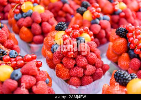 Plastikpunette aus Himbeeren, Erdbeeren, Rotkräuseln, Brombeeren, Physalis und anderen Früchten zum Verkauf in einem Obstladen. Stockfoto