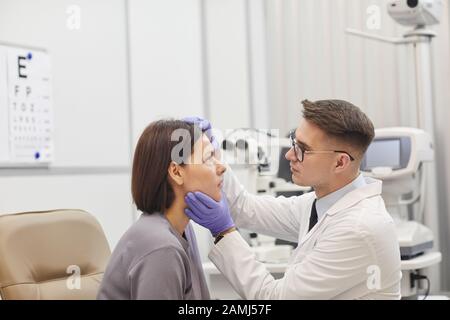 Seitenansicht des Portraits junger Augenarzt, das die Augen weiblicher Patienten öffnet, während sie ihre Sehkraft in der medizinischen Klinik überprüft, kopieren Sie den Raum Stockfoto