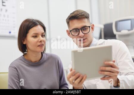 Portrait junger Augenarzt, der digitale Tablette verwendet, während der Untersuchung der Sehkraft bei Frauen in der modernen Klinik Stockfoto