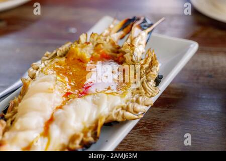 Nahansicht auf einem Gegrillten Giant River Prawn mit voller Rehe und fetter Garnele auf weißem Teller auf rauem Holztisch. Stockfoto