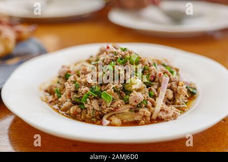Nahaufnahme von Larb, thailändischem Würzigen Hackfleisch oder Duckensalat, auf Holztisch und verwischter Hintergrund eines anderen Gerichts. Stockfoto