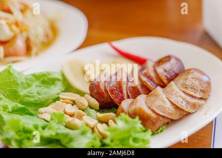 Nahansicht von Slice Gegrillter thailändischer nordöstlicher Wurst auf weißem Teller mit Erdnuss und Ingwer seitlich. Stockfoto