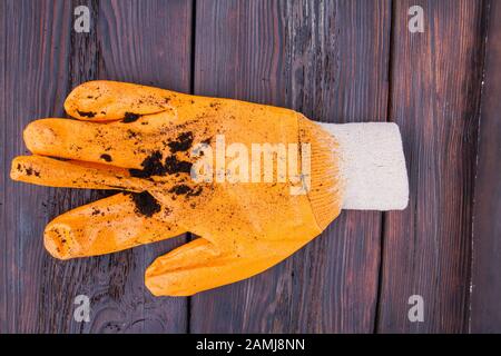 Orangefarbener Gartenhandschuh mit Bodenbeschmutzen nach harter Arbeit. Stockfoto