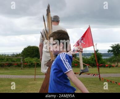 Ein kleiner Junge, der lernt, eine Axt auf ein lebendiges Geschichtsereignis zu werfen Stockfoto