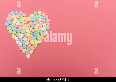 Bunte, herzförmige Süßigkeiten auf der rosafarbenen Oberfläche, valentinstags-liebeskonzept Stockfoto