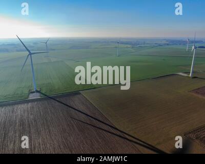 Luftbild von Windkraftanlagen auf landwirtschaftlichen Feldern während des blauen Wintertags. Energieerzeugung mit sauberer und erneuerbarer Energie. Stockfoto