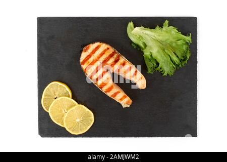 Gebratenes Lachssteak mit Zitrone und Salat auf Schiefer. Auf weissem Hintergrund Stockfoto