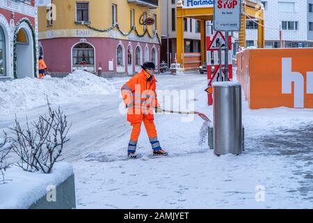 St. Moritz, Schweiz - 22. Dezember - Straßenaufräumer in hellorangefarbenem Mantel schneit an einer Straße in St. Moritz, Schweiz, Schnee von der Straße Stockfoto